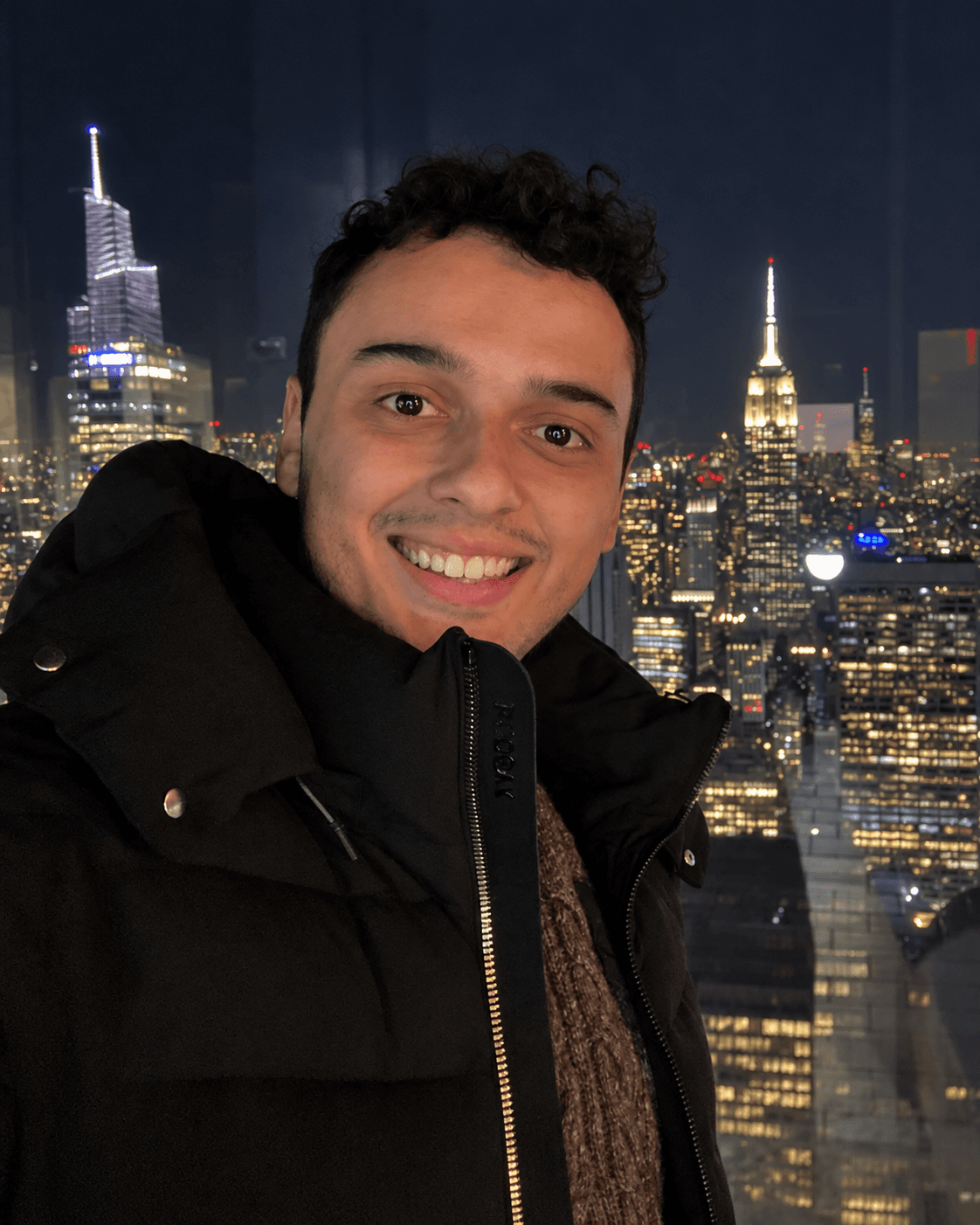 Jesus Martinez smiling in front of the New York City skyline at night